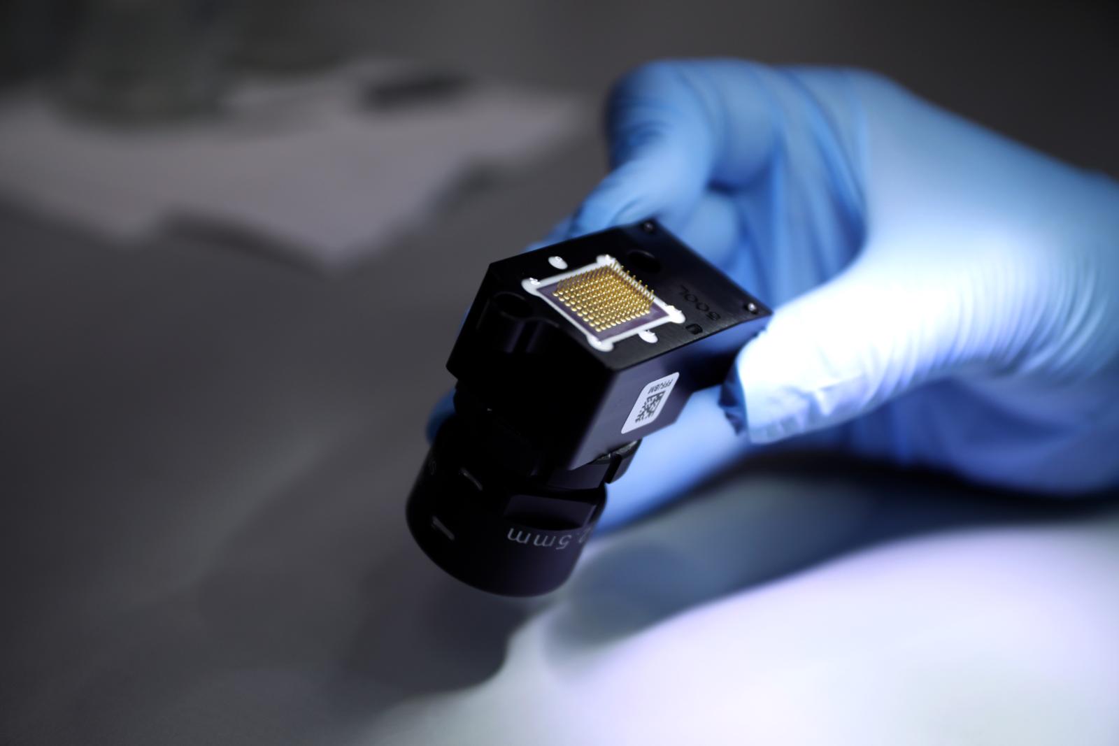 FISBA Mitarbeiter hält ein fertiges Objektiv in den Händen (Objektiv mit diversen Linsen/Optiken, Elektronik, Mechanik & Sensor)